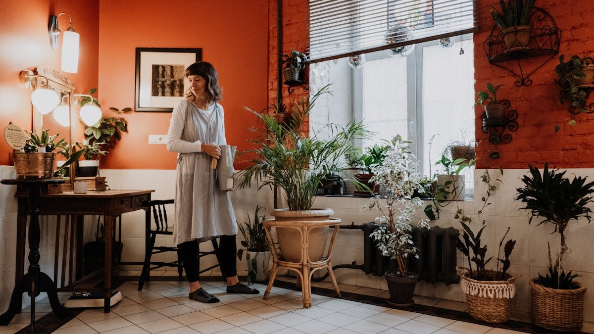 Woman arranging indoor plants in a stylish, warm-toned room.