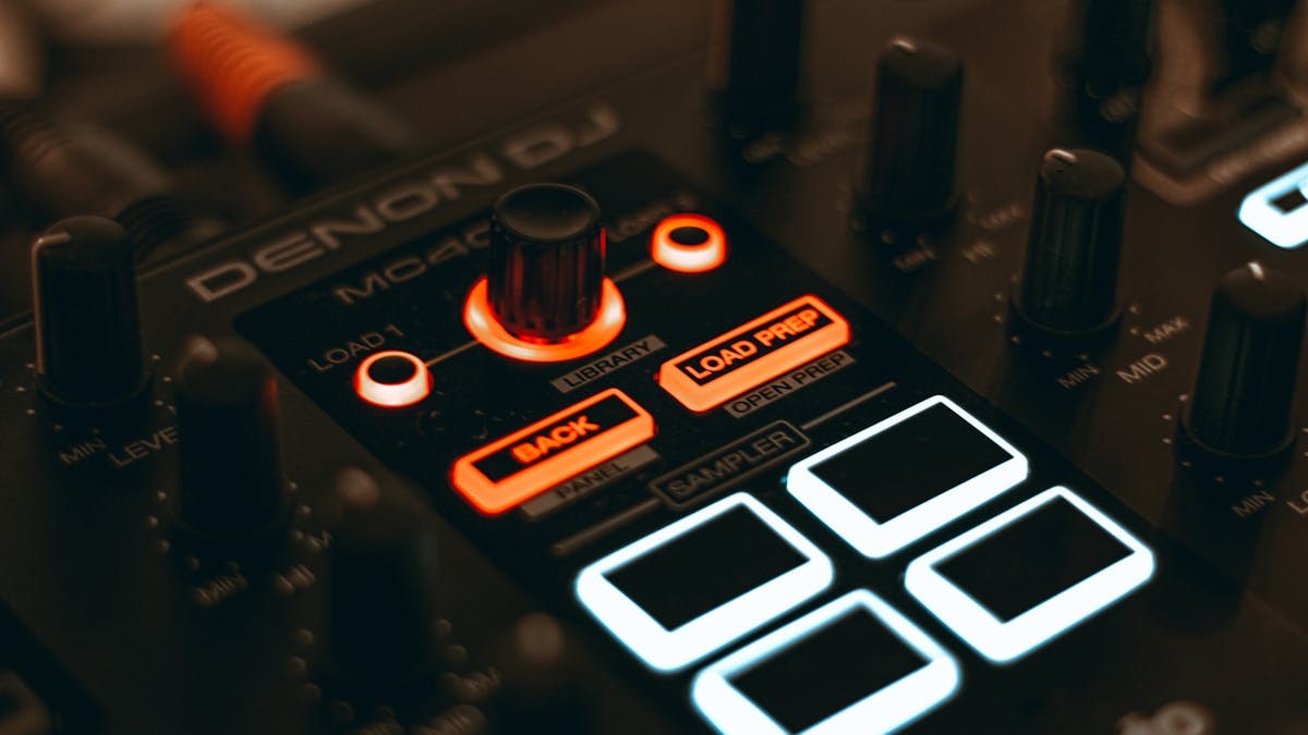 A detailed close-up of a DJ audio mixer with illuminated LED buttons and knobs.